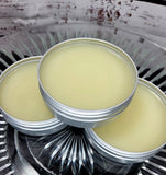 Three metal tins of beard balm on a decorative surface.