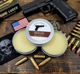 Two tins of 9mm Beard Balm with a gun, bullets, and American flag on a wooden surface.
