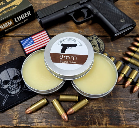 Two tins of 9mm Beard Balm with a gun, bullets, and American flag on a wooden surface.