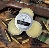 Carbine Beard Balm tins on a wooden surface with bullets and a rifle.