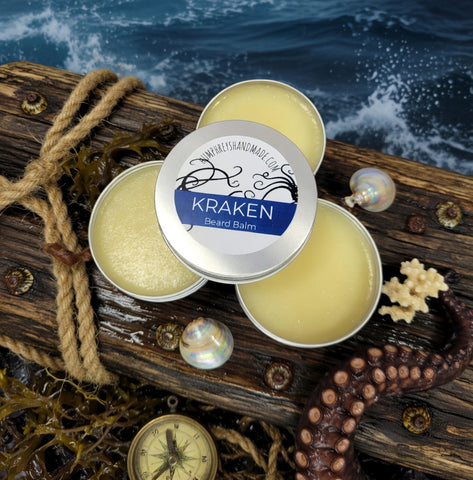 Three tins of Kraken Beard Balm on a wooden surface with ocean background
