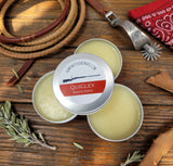 Quigley beard balm tins on a wooden surface with rustic items.