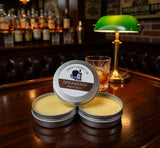Speakeasy beard balm tins on a bar counter with a lamp and bottles in the background