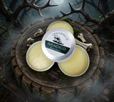 Three tins of Wendigo Beard Balm on a wooden surface with antlers and bones in the background.