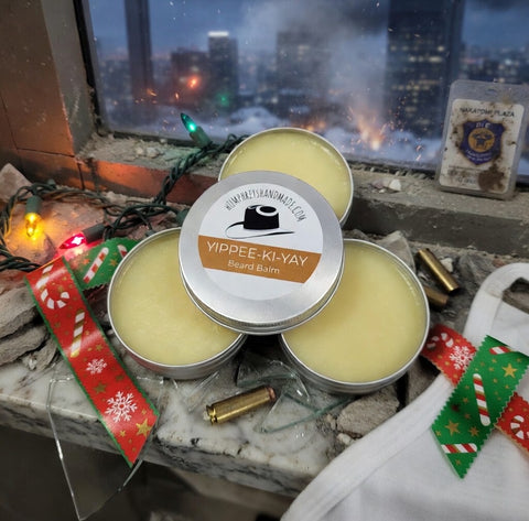 Three tins of Yippee-Ki-Yay beard balm on a ledge with a cityscape background.